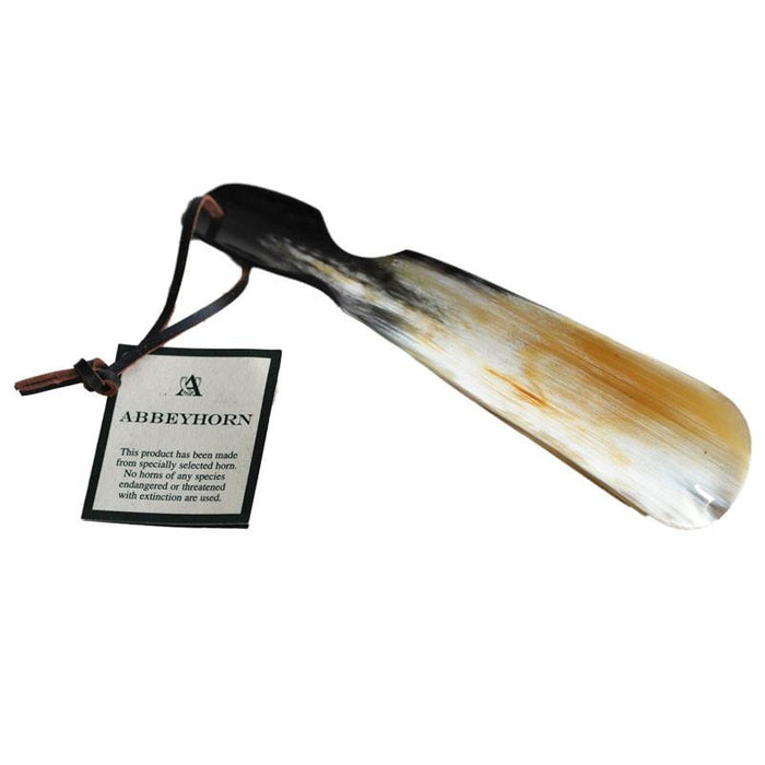 A flat-shaped shoe horn with a cut-out handle and a leather thong strap, made of natural horn, with a product label attached.