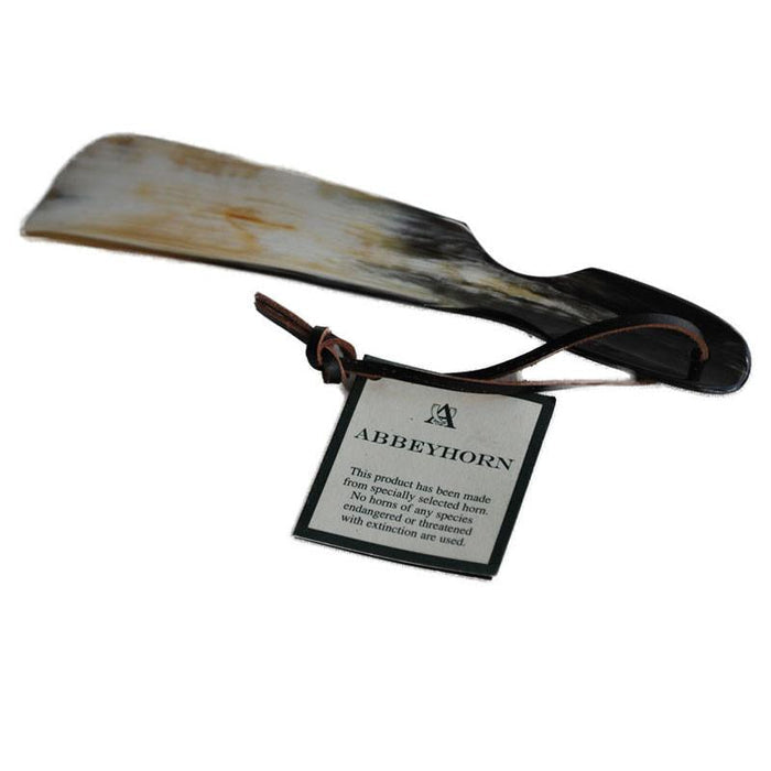 A flat-shaped shoe horn with a cut-out handle and a leather thong strap, made of natural horn, with a product label attached.