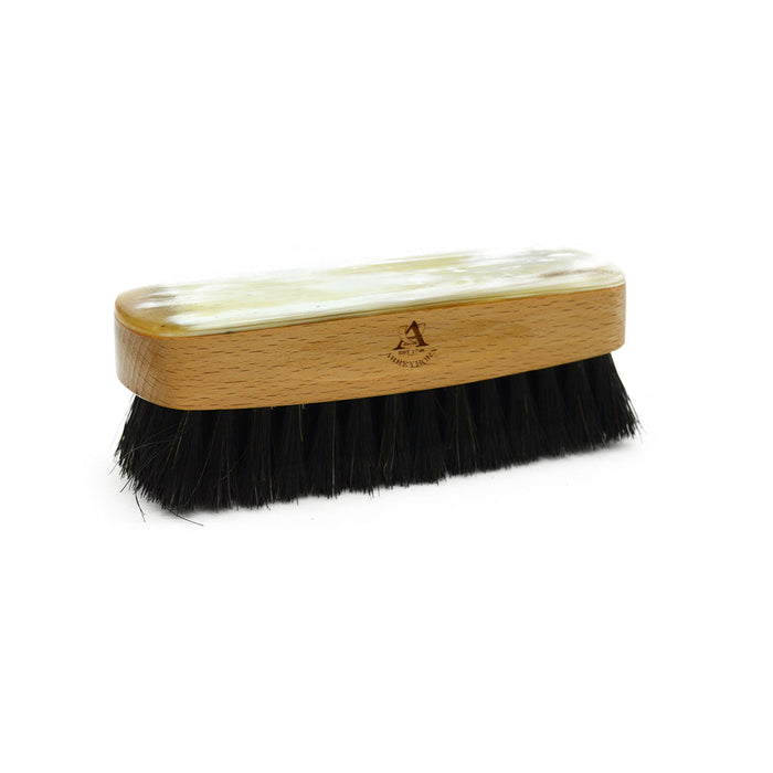 A handcrafted shoe polishing brush with a black and white oxhorn handle and dark bristles, presented on a plain background.