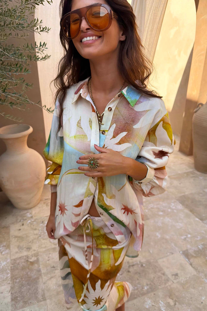 Abstract Soleil Marley Shirt with multicoloured sun motifs and oversized silhouette, worn with large sunglasses.
