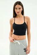A woman stands against a plain white background wearing the SPLITS59 Airweight Crop - Black paired with light gray sweatpants featuring a "56" on the left, perfect for hot yoga.