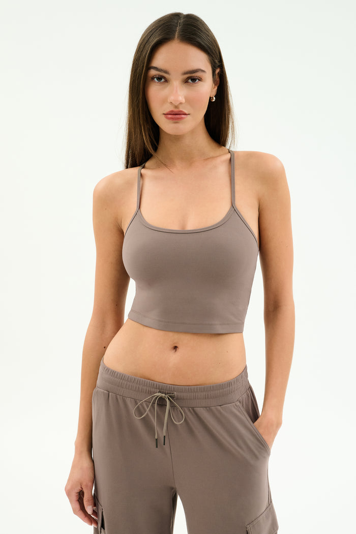 A woman with long brown hair models the SPLITS59 Airweight Crop in Lentil, paired with matching drawstring pants, standing against a plain light background.