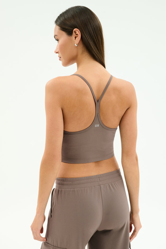 A woman with long brown hair stands against a plain light background wearing the SPLITS59 Airweight Crop in Lentil, paired with matching pants—perfect for hot yoga or any workout.