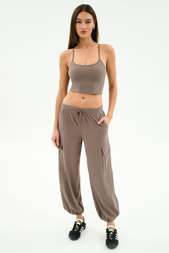 A woman faces forward wearing the SPLITS59 Airweight Crop in Lentil with matching taupe cargo pants and black sneakers against a white background—ideal for hot yoga or casual outings.