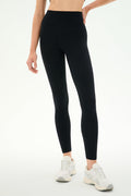 A person wearing SPLITS59 Airweight High Waist Legging in black and white athletic shoes stands against a plain light background, ready for hot yoga.