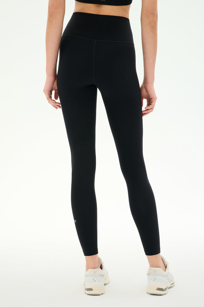 Model wearing SPLITS59 Airweight High Waist Legging in Black with white sneakers, shown from the back against a plain white background—ideal for hot yoga sessions.