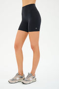 A person in SPLITS59 Airweight High Waist Shorts - Black and gray sneakers stands against a white background, ready for pilates or hot yoga.