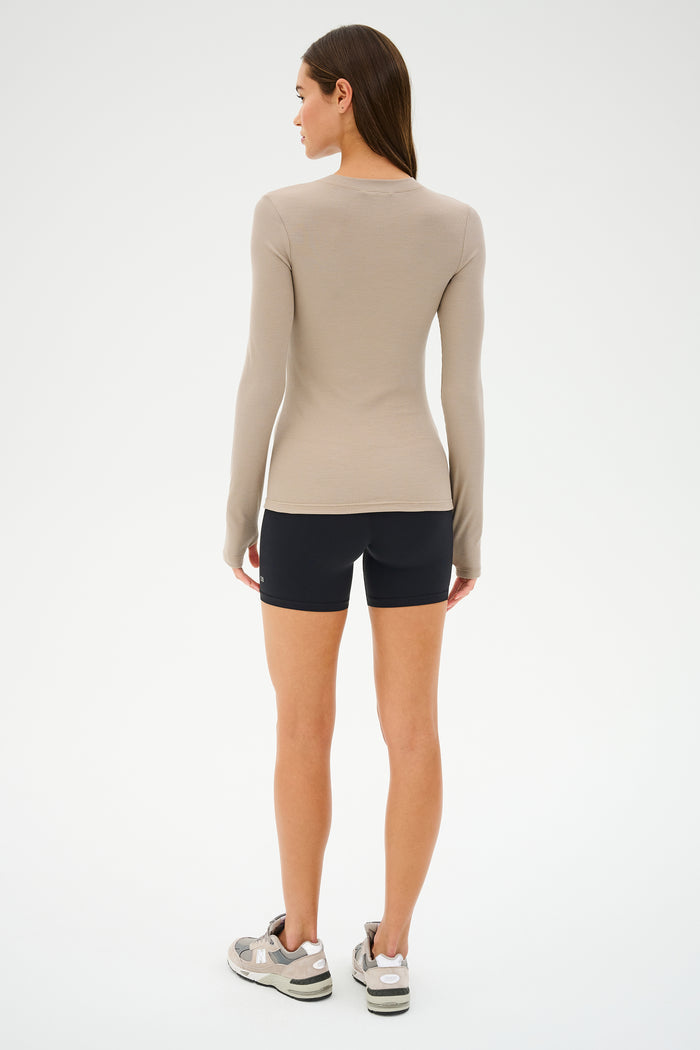 A person with long hair faces away in a beige long-sleeve top, wearing SPLITS59's Airweight High Waist Short in black and sneakers, set against a plain white background.
