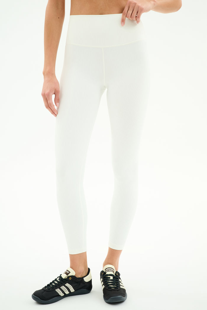 Person wears SPLITS59 Airweight Rib High Waist 7/8 leggings in white with black Adidas sneakers, standing against a plain white background. Upper body partially out of frame—ideal for Pilates or hot yoga.