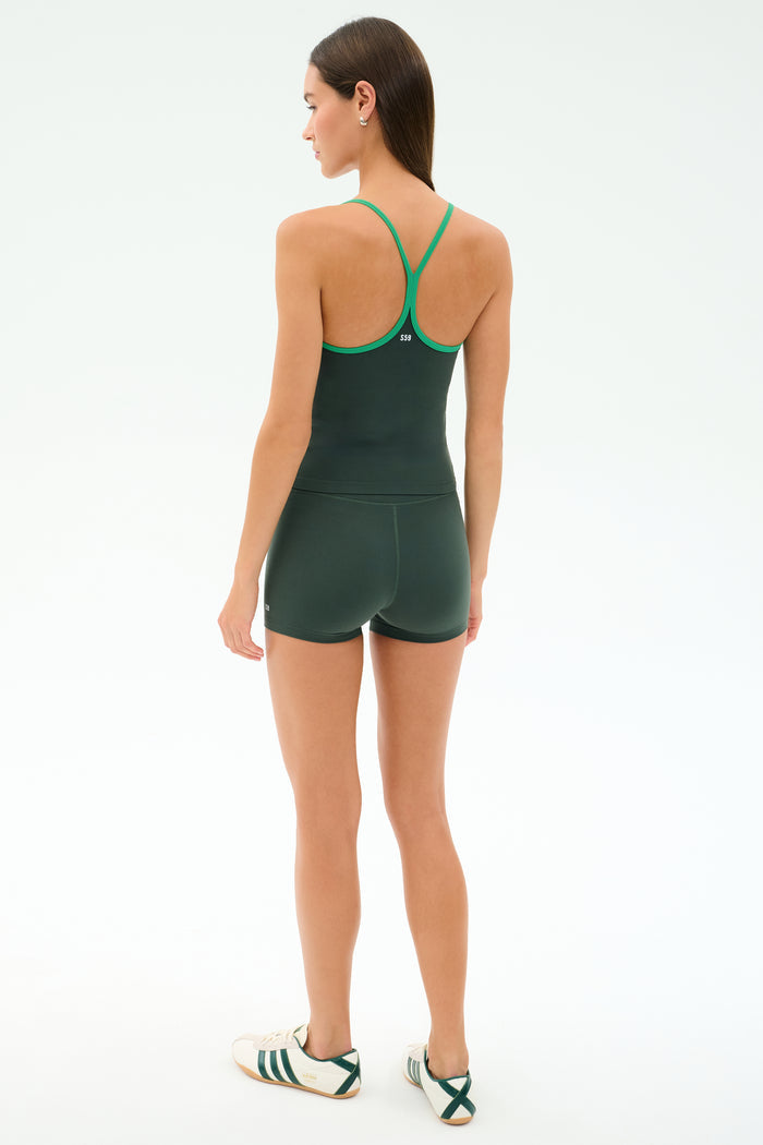 A woman faces away, wearing the SPLITS59 Airweight Tank in Military/Spearmint with matching shorts and white sneakers, set against a plain light background.
