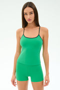 A woman faces forward in a plain white setting, wearing the SPLITS59 Airweight Tank in Spearmint/Military with matching shorts—green activewear crafted from stretch fabric.