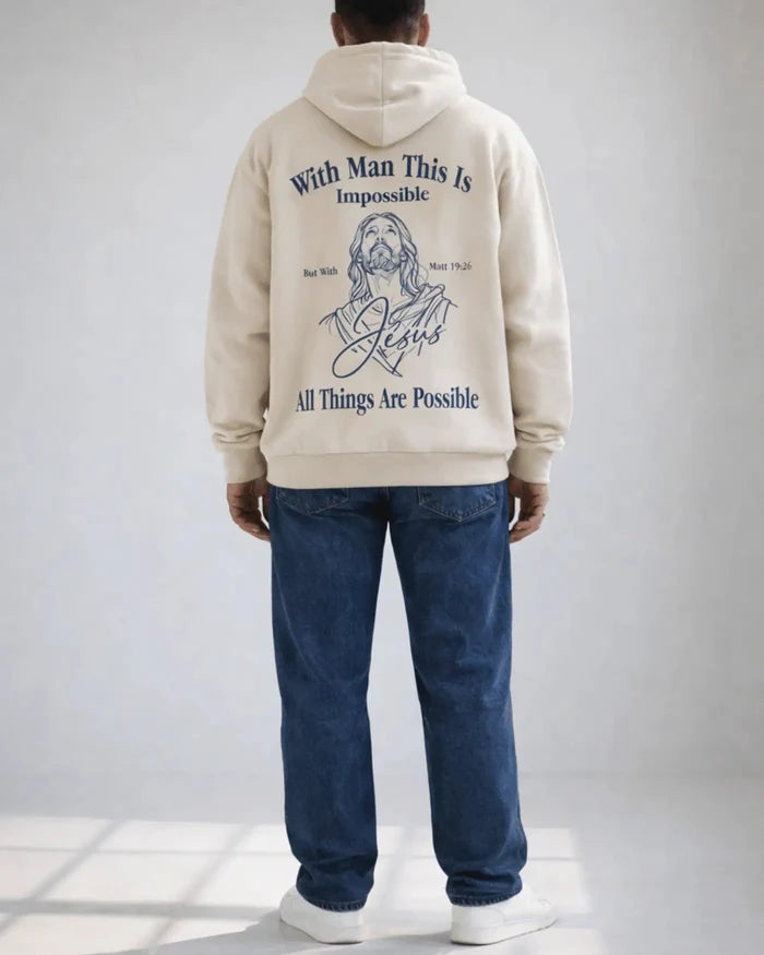 Person wearing a beige hoodie with text and a graphic of a religious figure on the back, standing against a plain background.