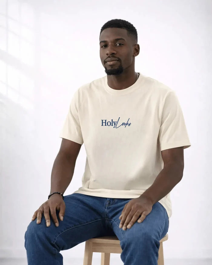 Man wearing a beige t-shirt with 'Holy Loaf' logo sitting on a stool against a white background
