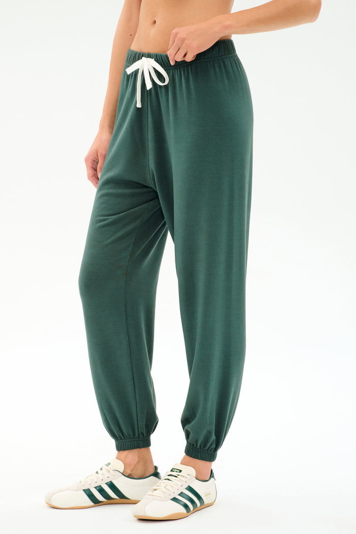 Wearing the SPLITS59 Andie Oversized Fleece Sweatpant in Military, styled with white sneakers featuring green stripes—perfect for cool weather workouts—standing against a plain white background.