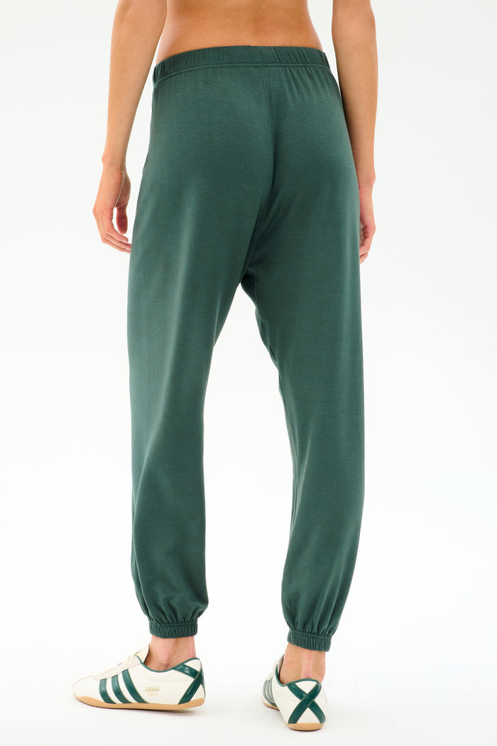 Person wearing SPLITS59 Andie Oversized Fleece Sweatpant in Military and white sneakers with green stripes, shown from the back on a plain white background—ideal for cool weather workouts or laid-back days.