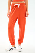 A person wears the SPLITS59 Andie Oversized Fleece Sweatpant in Valencia with a white drawstring and white sneakers, standing against a plain light background.