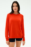 A person with long dark hair wears the SPLITS59 Andie Oversized Fleece Sweatshirt in Lotus Red and black shorts, standing against a plain light background.