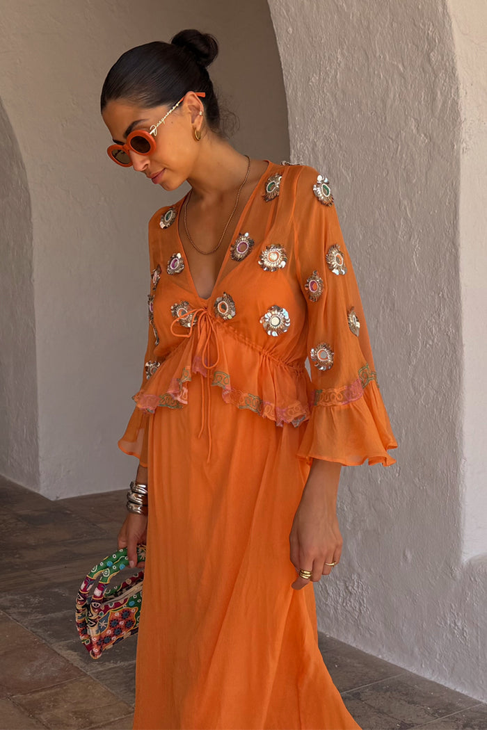 Apricot Embellished Ines Dress in orange with mirror detailing and a peplum hem, styled in a stone archway.