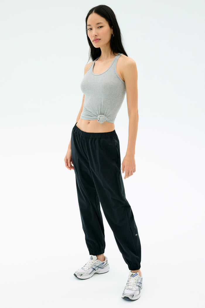 A woman faces forward, wearing the Splits59 Ashby Rib Tank in Lt. Heather Grey, paired with black jogger pants and white athletic sneakers, set against a plain white background.