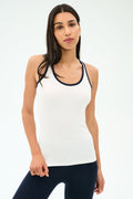 A woman stands against a plain background wearing the SPLITS59 Ashby Rib Tank in White/Indigo with dark pants, looking at the camera—an ideal outfit for yoga or gym sessions.