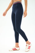 A person wearing SPLITS59 Bailey High Waist Active Rib 7/8 leggings in Heather Indigo with a striped waistband and white sneakers with red stripes, standing against a plain background—ideal for gym workouts.