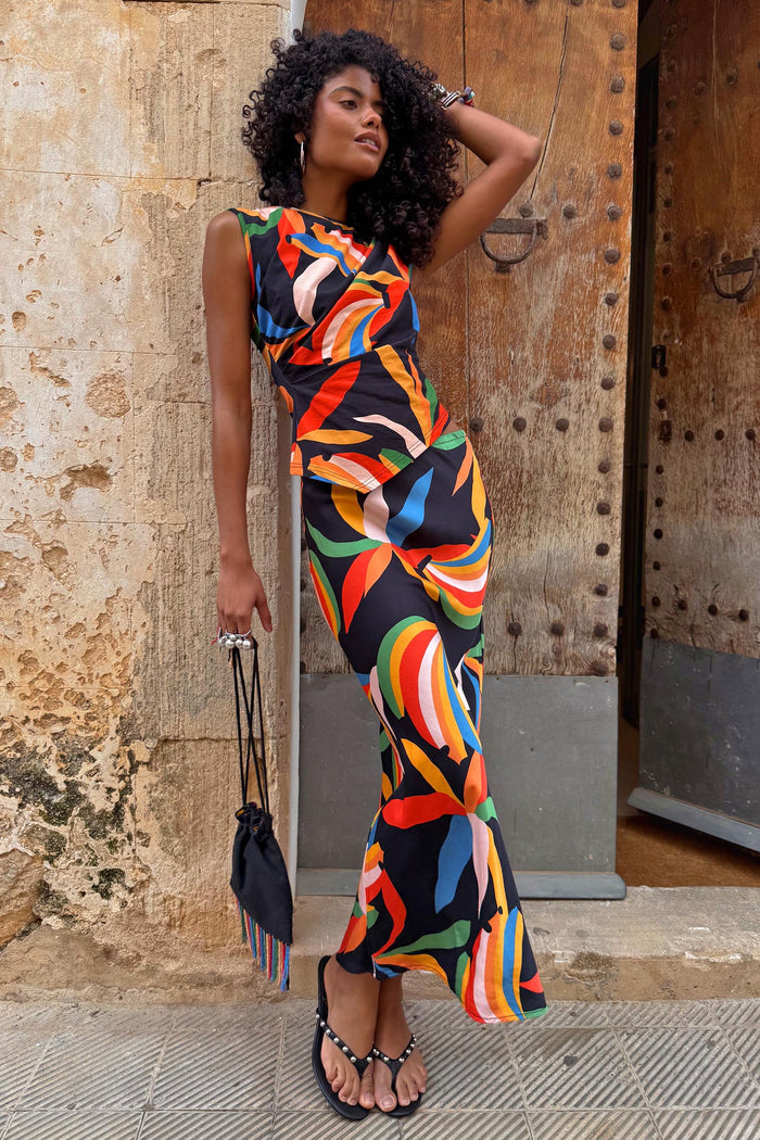 Banana Dorris Skirt in a multicoloured hand-painted banana print on black jersey, styled as a co-ord against a stone wall.