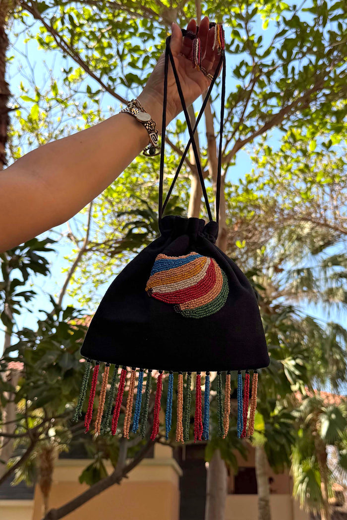 Black cotton Banana Pouch Bag with a beaded banana motif and multicolour tassel fringe, held outdoors.