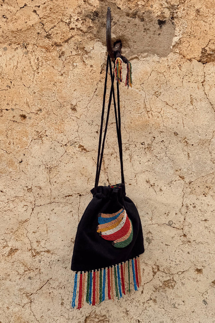 Black Banana Pouch Bag with a colourful beaded banana motif and multicolour fringe hanging on a rustic stone wall.