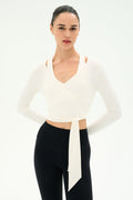A woman wears the SPLITS59 Bella Airweight Lite Wrap in white paired with black high-waisted nylon-spandex leggings, standing against a plain light background.