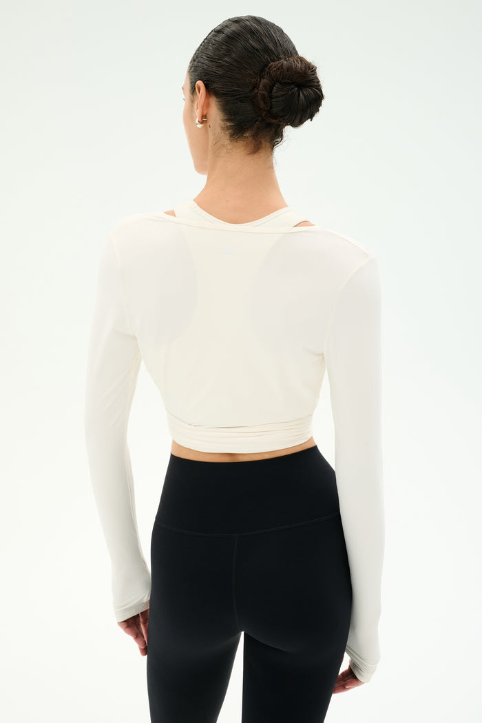 A woman with dark hair in a bun models the SPLITS59 Bella Airweight Lite Wrap in white, standing with her back to the camera against a plain white background.