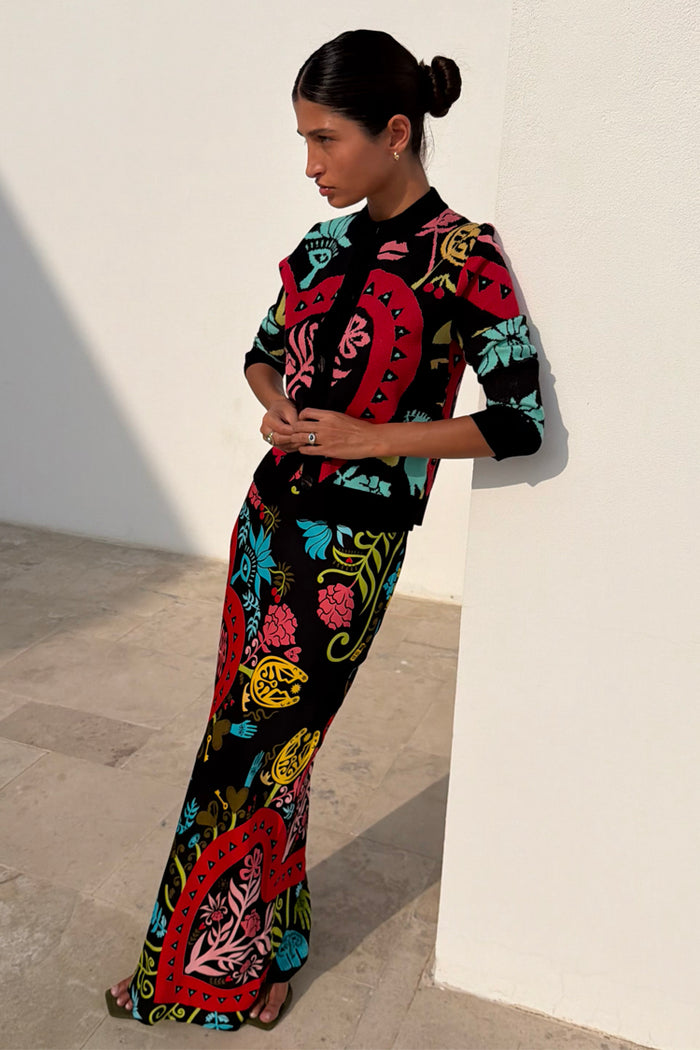 Black Amara Hollie Cardigan with heart and eye motifs, paired with a matching printed skirt against a wall.