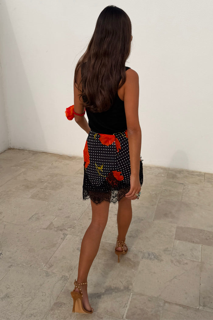 Black Poppy Mini Maeva Skirt featuring a polka dot and poppy floral print with a delicate lace hem, seen from behind.
