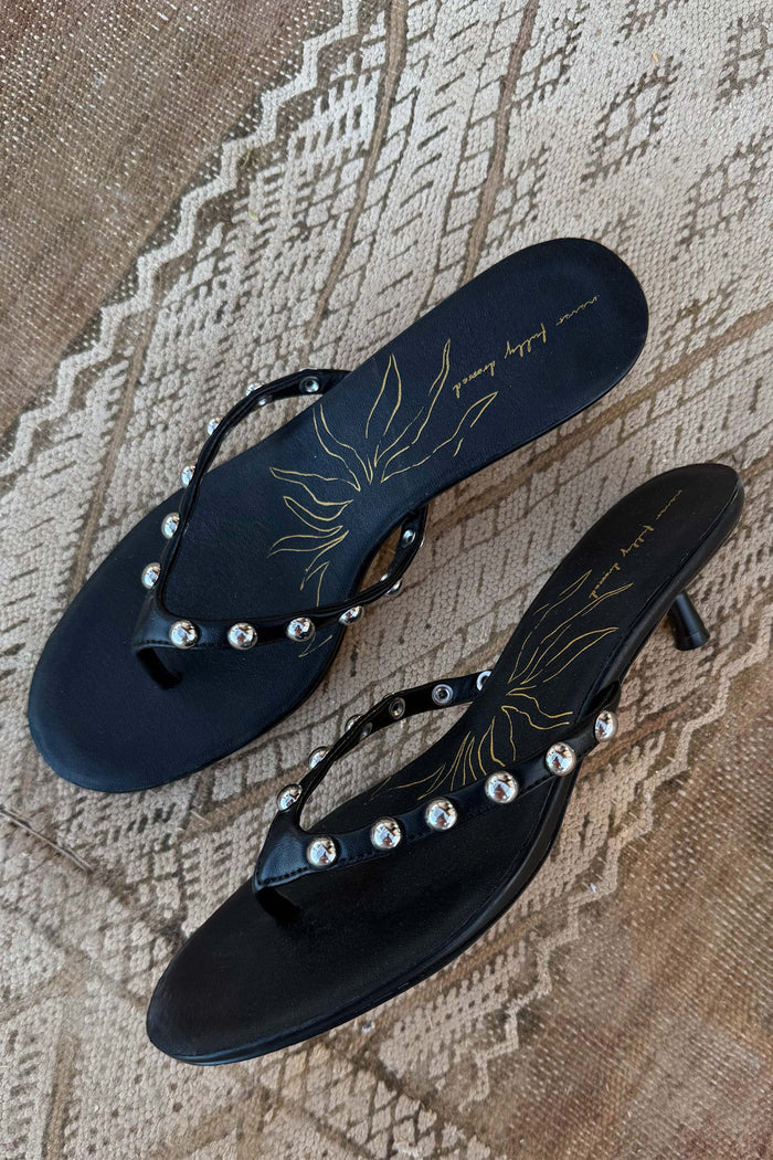 Black Stud Sandal Mules in leather with silver studs, a low kitten heel and signature sun motif on a patterned rug.