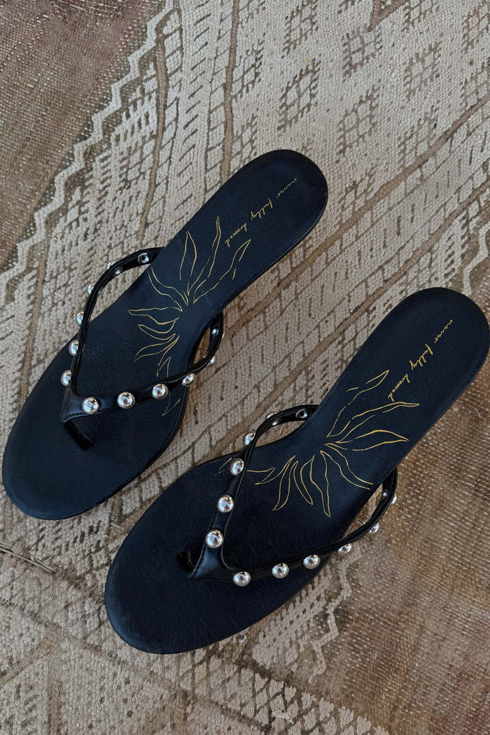 Black leather stud sandal mules with silver detailing and a gold sun motif, displayed top-down on a woven rug.