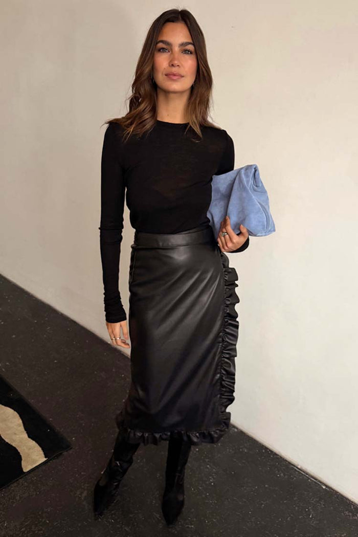 Black Vegan Leather Ruffle Jaspre Skirt featuring side frills, paired with a black long-sleeve top and blue clutch.
