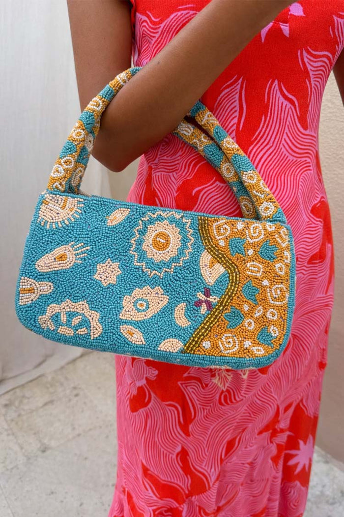 Blue and Yellow Morocco Beaded bag with hand-embellished gold motifs, held by a model in a pink patterned dress.