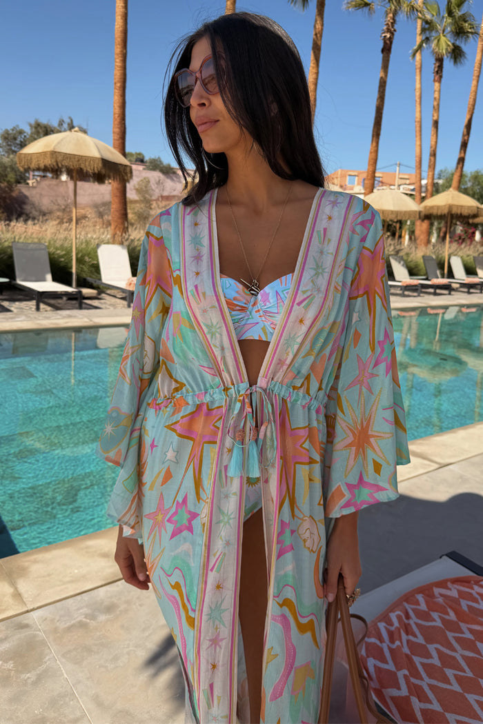 Blue Dreamer Maxi Kimono in light blue with star and heart motifs, styled poolside with a tie waist and tassels.
