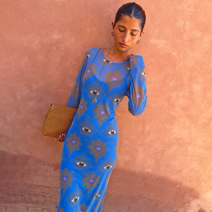 Blue Eye Mesh Dress with eye and heart motifs, a long-sleeved fitted maxi silhouette and tan clutch for vacation.