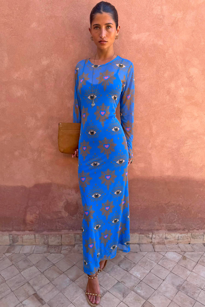 Blue Eye Mesh Maxi Dress with pink heart and eye motifs and long sleeves, worn by a model against a terracotta wall.