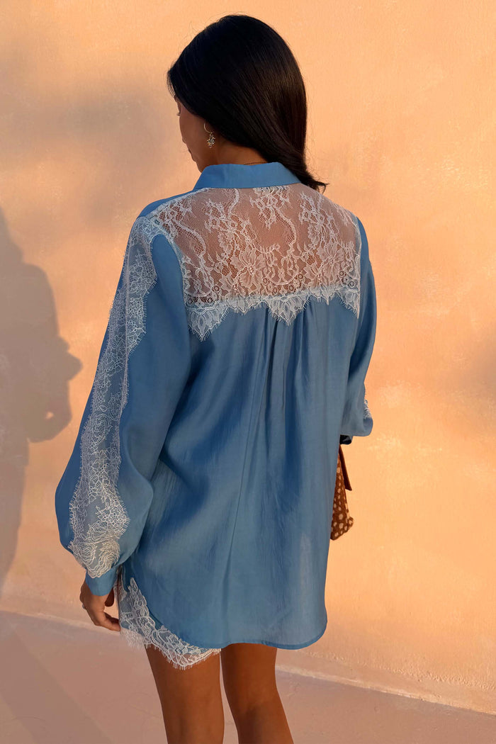 Blue Lace Marley Shirt with lace detailing on the back and sleeves, shown from a rear view against a peach wall.