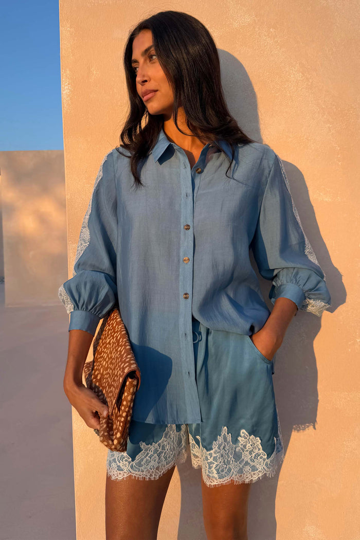 Blue Lace Marley Shirt with white lace detailing on sleeves, styled with matching lace shorts and a patterned clutch.