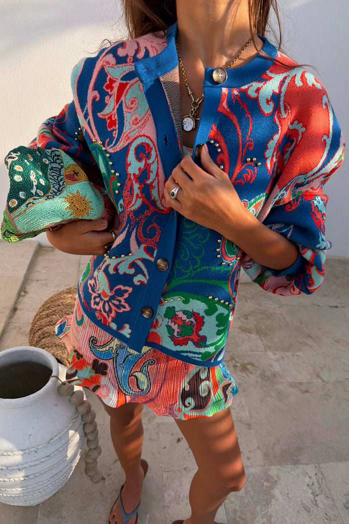 Blue Mari Cardigan featuring orange and turquoise paisley motifs and gold stud details, styled as a wardrobe staple.