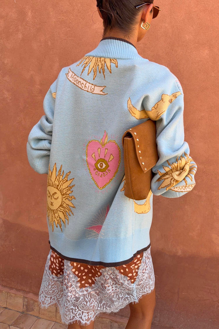 Blue Mystical Cardigan featuring sun and moon jacquard motifs, a pink heart and 'Moonchild' banner on the back.