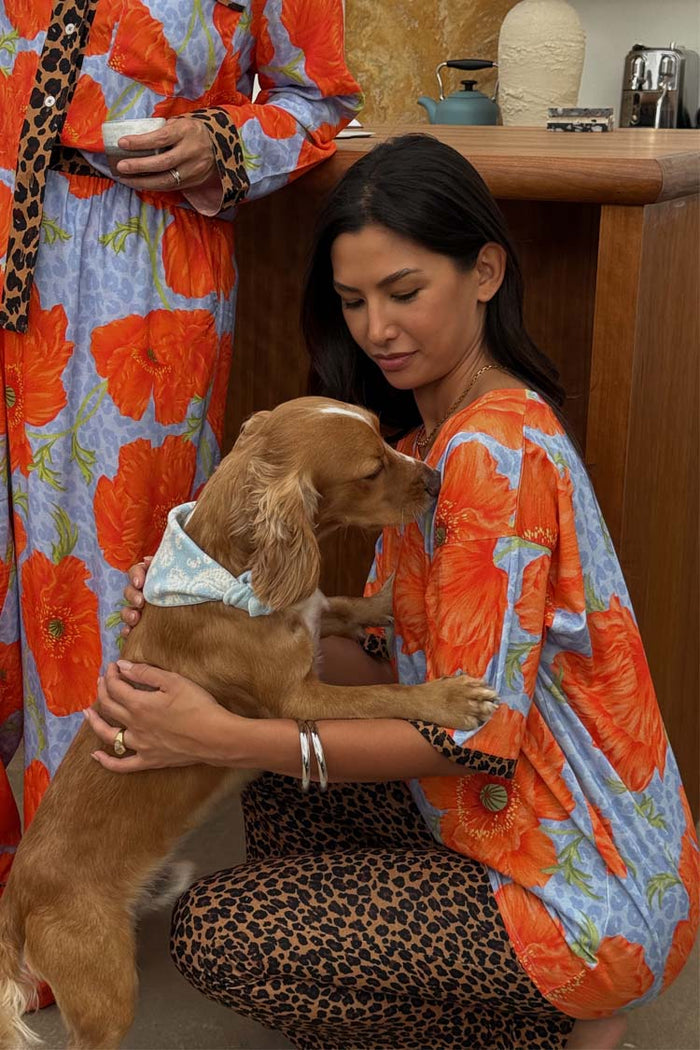 Blue Poppy Print Jersey Pyjamas with orange poppies and leopard trim, worn by a model cuddling a dog.