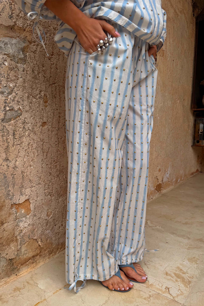 Blue and cream striped balloon trousers with gold stud detailing, voluminous cotton fit and adjustable tie cuffs.