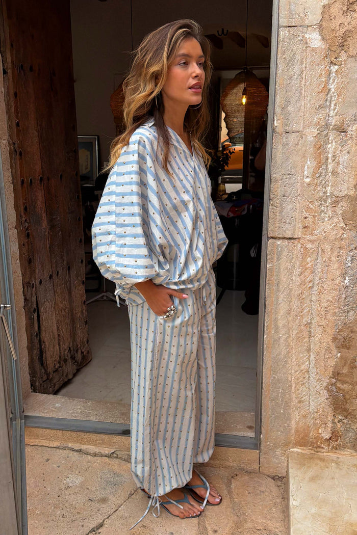Blue stripe balloon trousers with gold studs and tie-cuff hems, styled with a matching co-ord top on a model.
