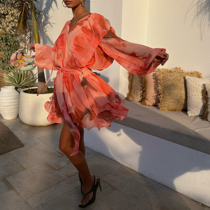 Peach orange Blurred Floral Ella Mini Dress with flute sleeves and a tiered ruffle skirt in an outdoor patio setting.