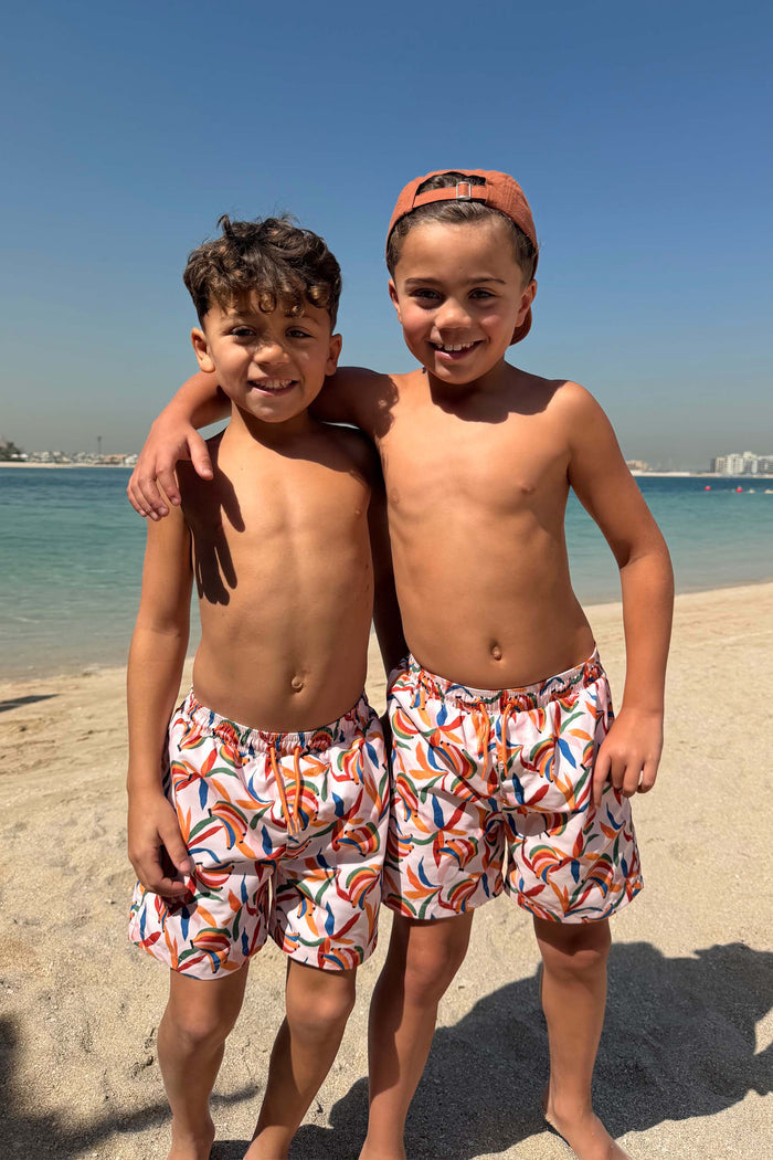 Cream Boy's Banana Print Swim Shorts in recycled fabric, worn by two boys on a sunny beach vacation.