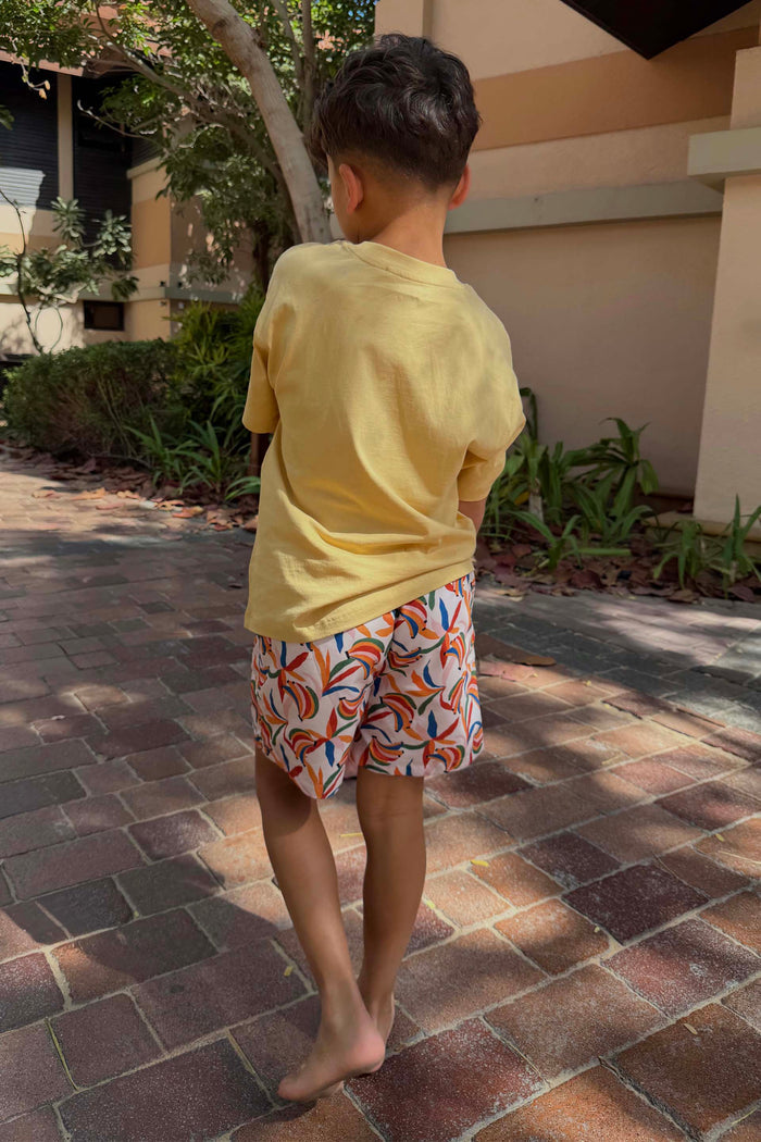 Boy's Banana Print Swim Shorts in cream with multi-coloured fruit, paired with a yellow tee for vacation.