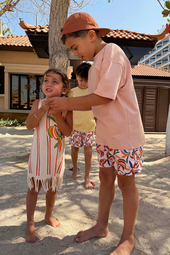 Boy's multi-coloured Banana Print Swim Shorts in recycled polyester, worn by children in a sunny vacation setting.